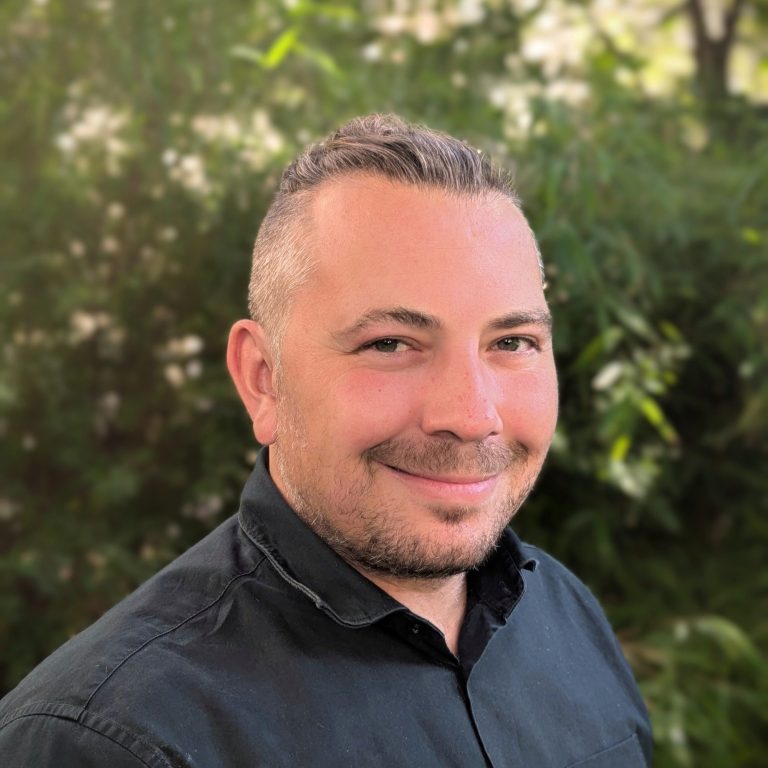 Porträt eines Mannes mit kurzem Haar, in einem hellen Hemd, neutralem Hintergrund.